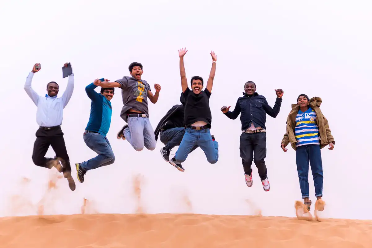 Original photo of six friends jumping on sand under a bright sky