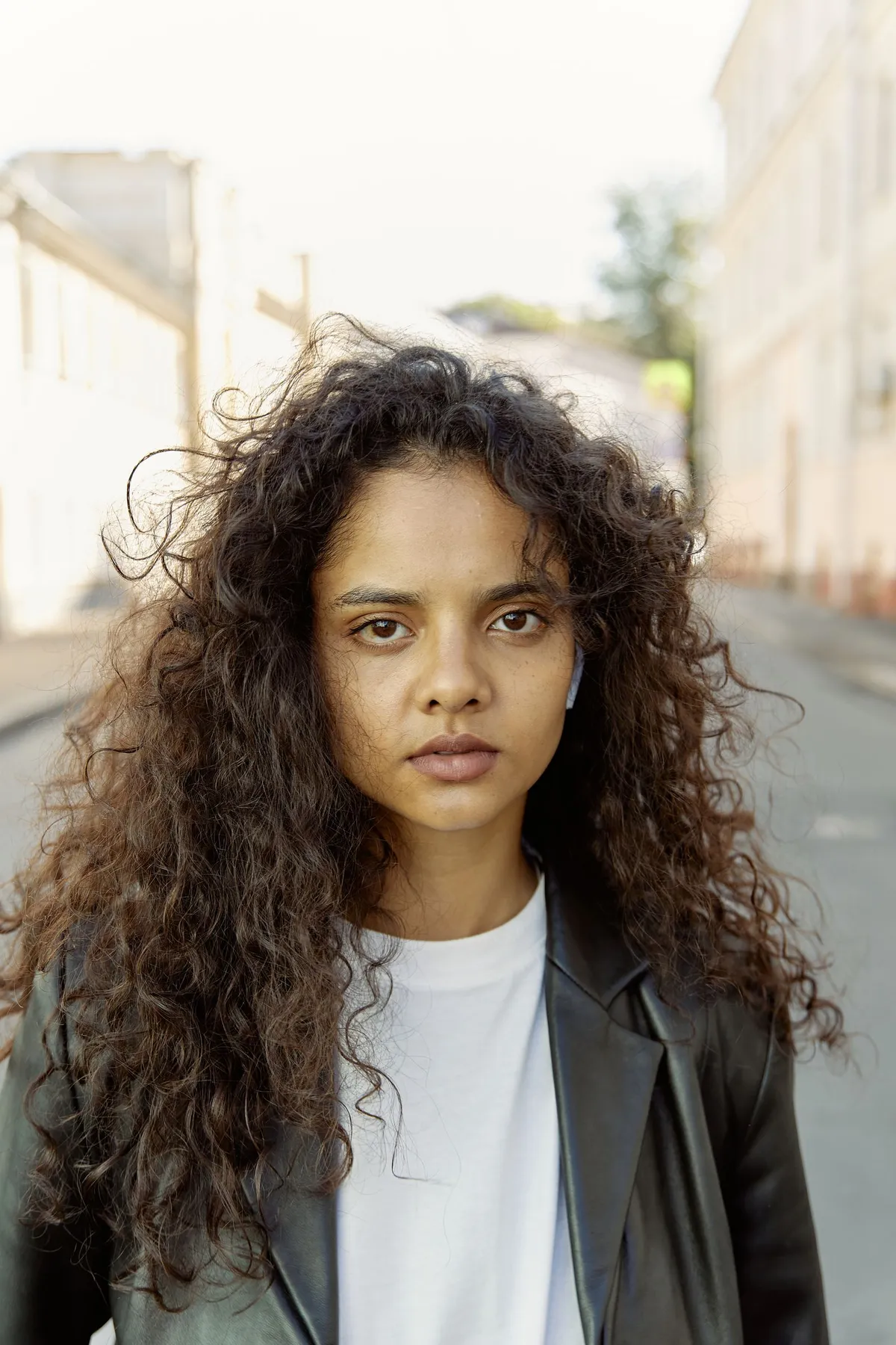 Original portrait photo of a woman with curly hair on a bright street