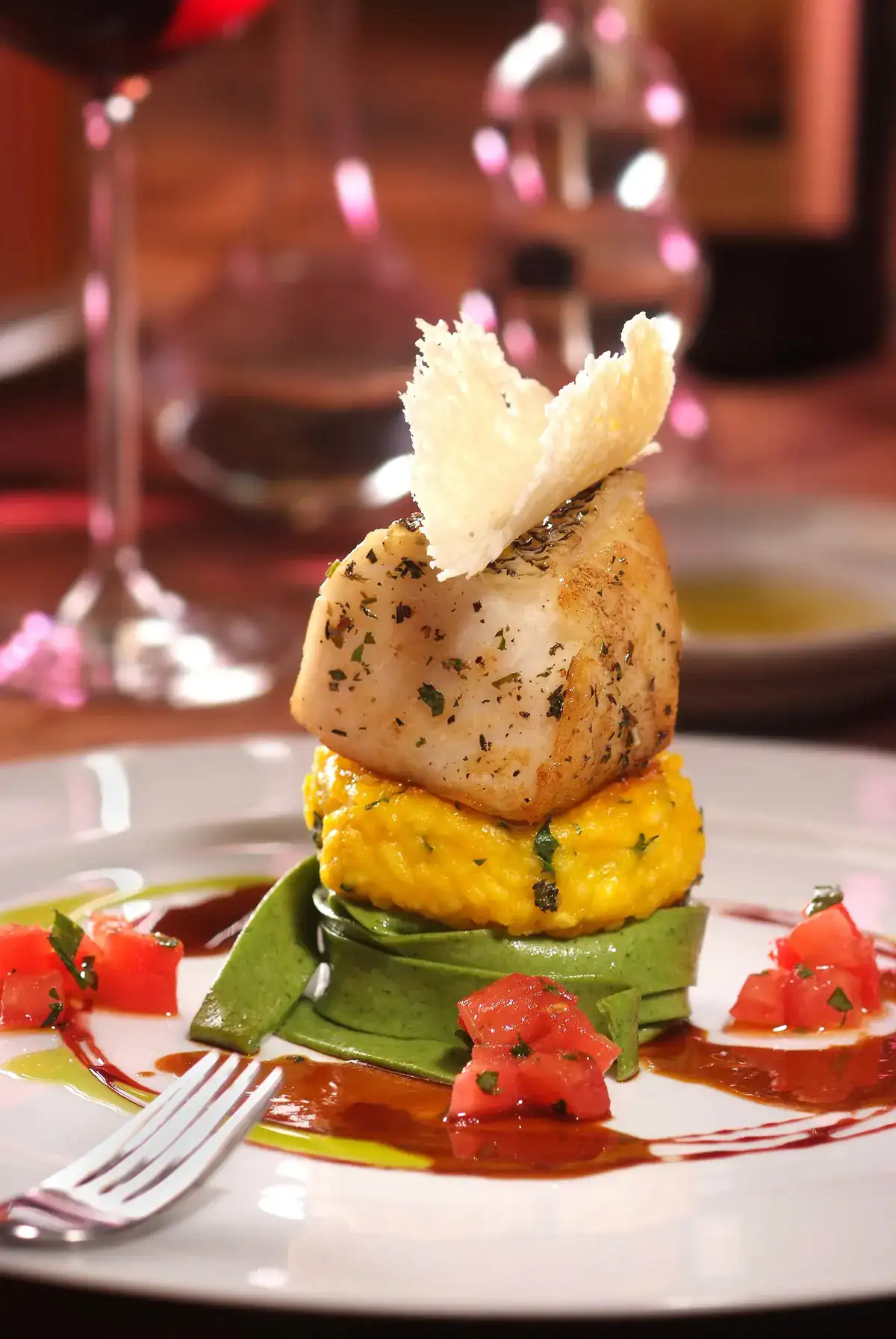 Original photo of a seared scallop stack with risotto and a tuile crisp on a restaurant table